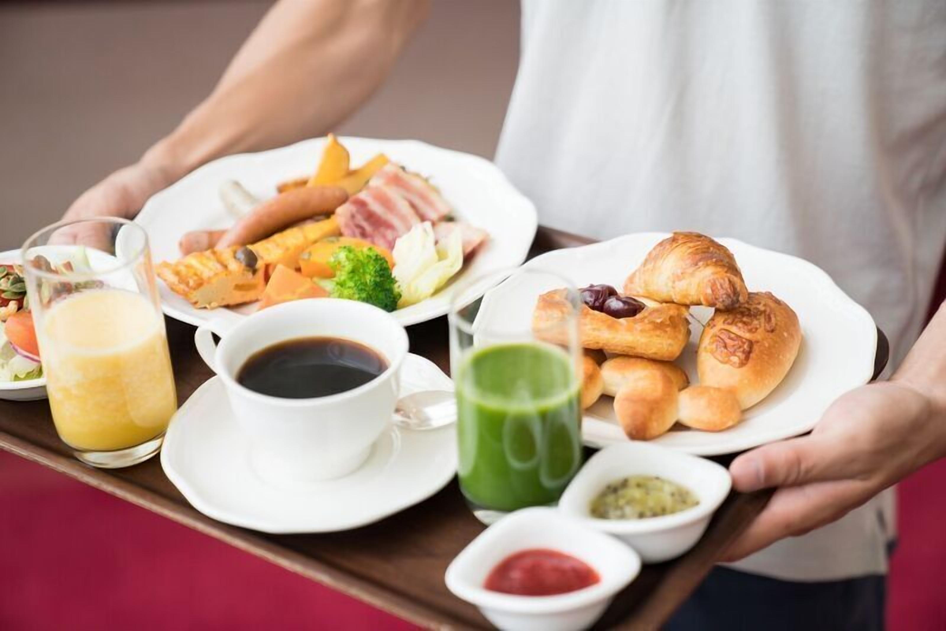 A tray with breakfast items including croissants, a green drink, and a plate with eggs and bacon.