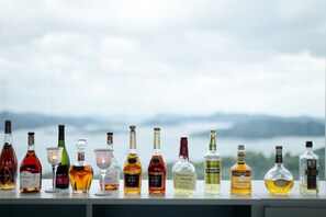 Une rangée de bouteilles d’alcool est alignée sur une étagère, avec un paysage montagneux en arrière-plan.