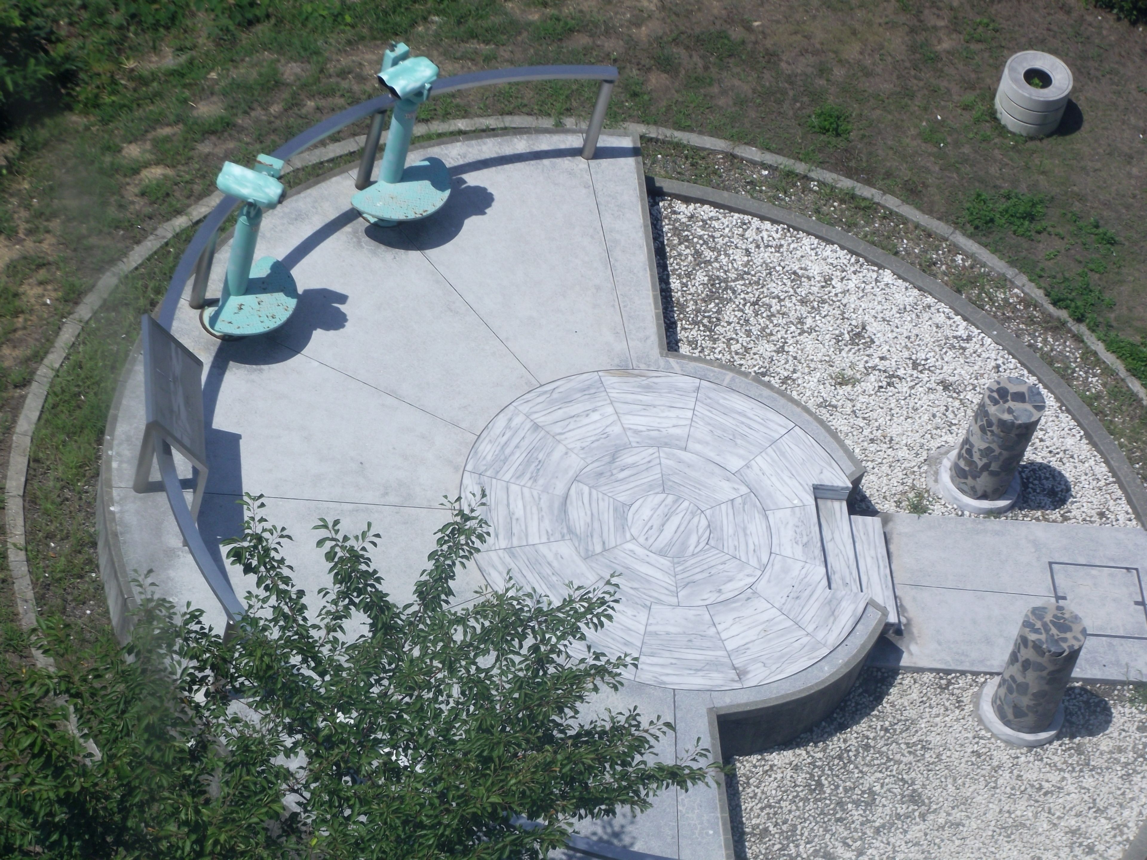 A circular outdoor area with a central mosaic pattern, surrounded by a low wall and benches.