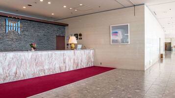 Zona de recepción de hotel con mostrador de mármol, alfombra roja, pared de piedra y un cuadro enmarcado.