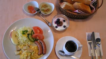 A breakfast plate with scrambled eggs, sausages, and vegetables, a bowl of yogurt with berries, a basket of bread, and a cup of coffee.