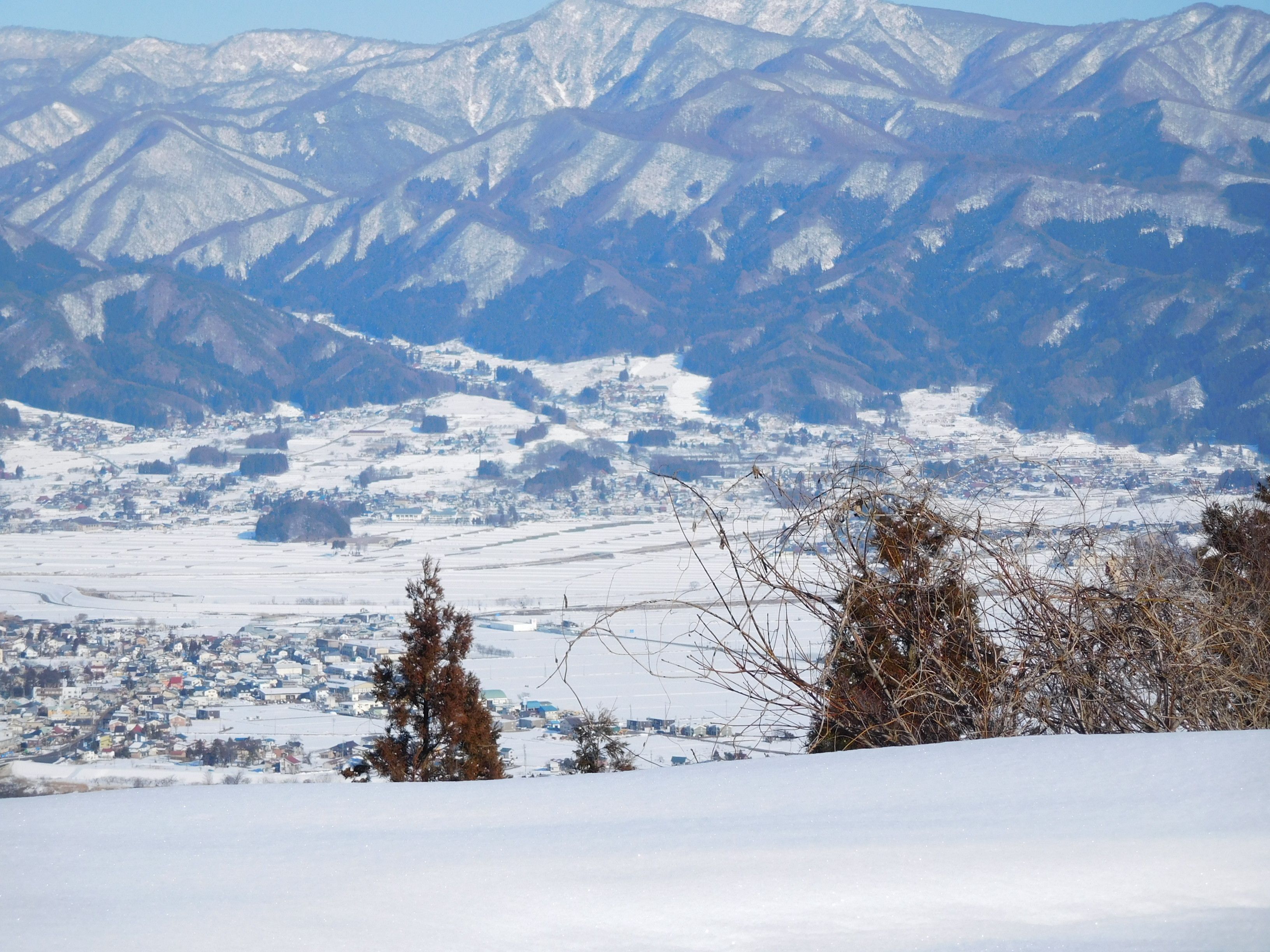 A snowy landscape with a town in the valley and mountains in the background.