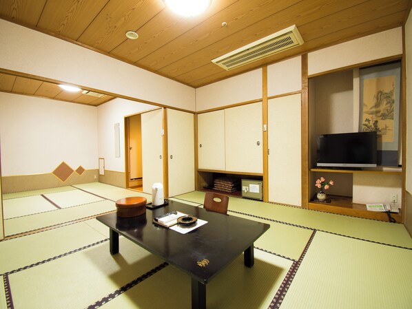 A tatami mat room with a table, chairs, a heater, a TV, and traditional Japanese artwork.