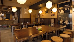 Interior de restaurante com mesas de madeira, banquetas de vime, lanternas de papel penduradas e diversas decorações nas paredes.