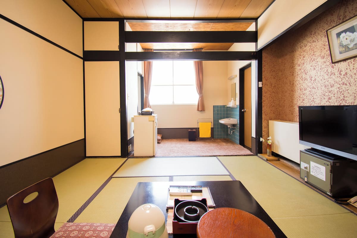 A traditional Japanese room with tatami flooring, a television, and a futon bed.