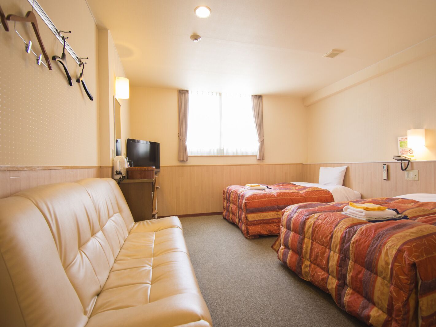 Ein Hotelzimmer mit einer Couch, zwei Betten, einem Fernseher und einem Fenster mit Vorhängen.