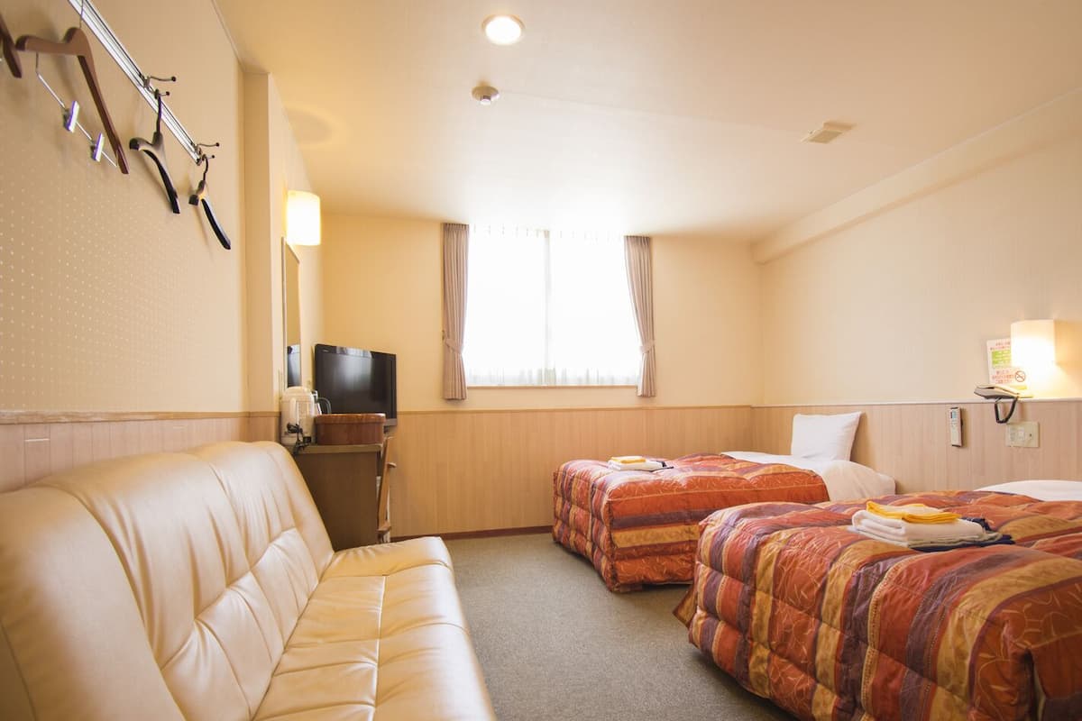 A hotel room with a sofa, two beds, a television, and a window with curtains.