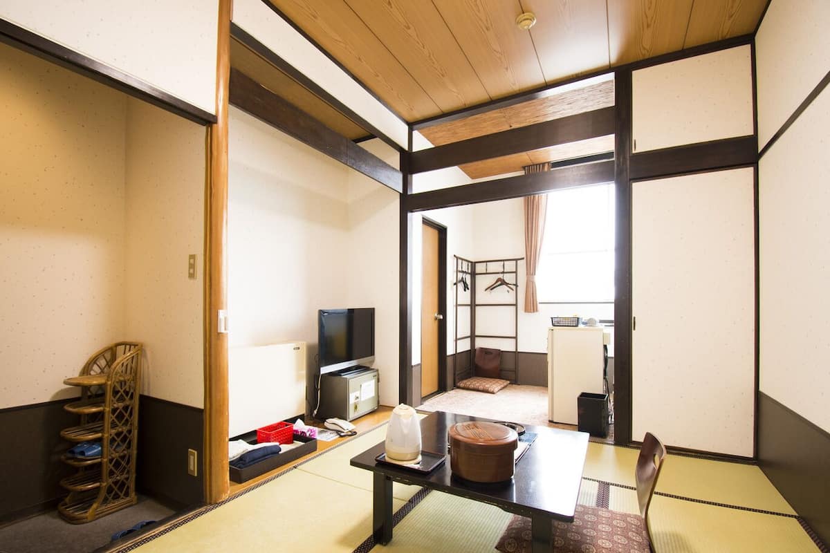 A traditional Japanese room with tatami flooring, a low table, a television, and a futon bed.