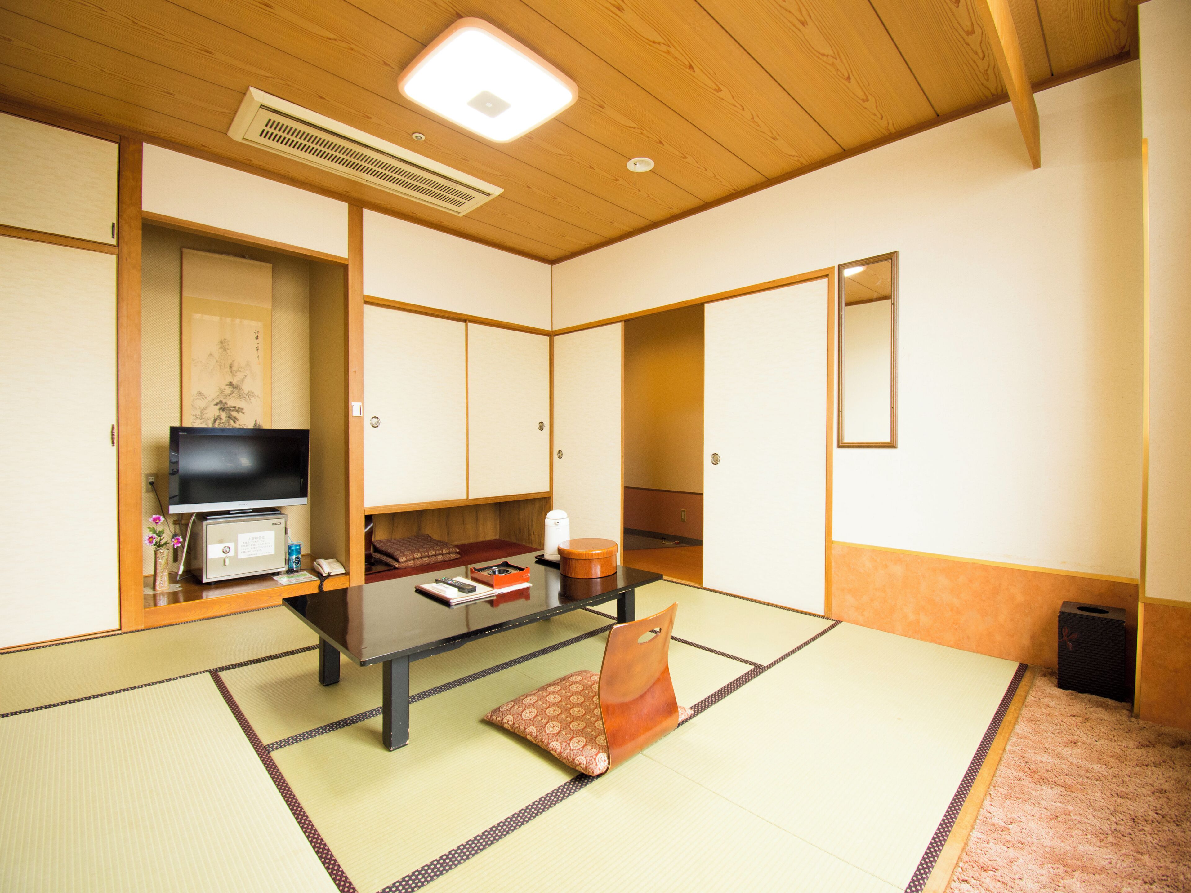 A traditional Japanese room with tatami flooring, a television, a table, and sliding doors.
