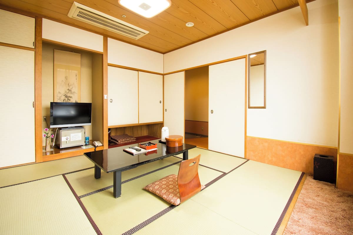 A traditional Japanese room with tatami flooring, a television, a table, and sliding doors.
