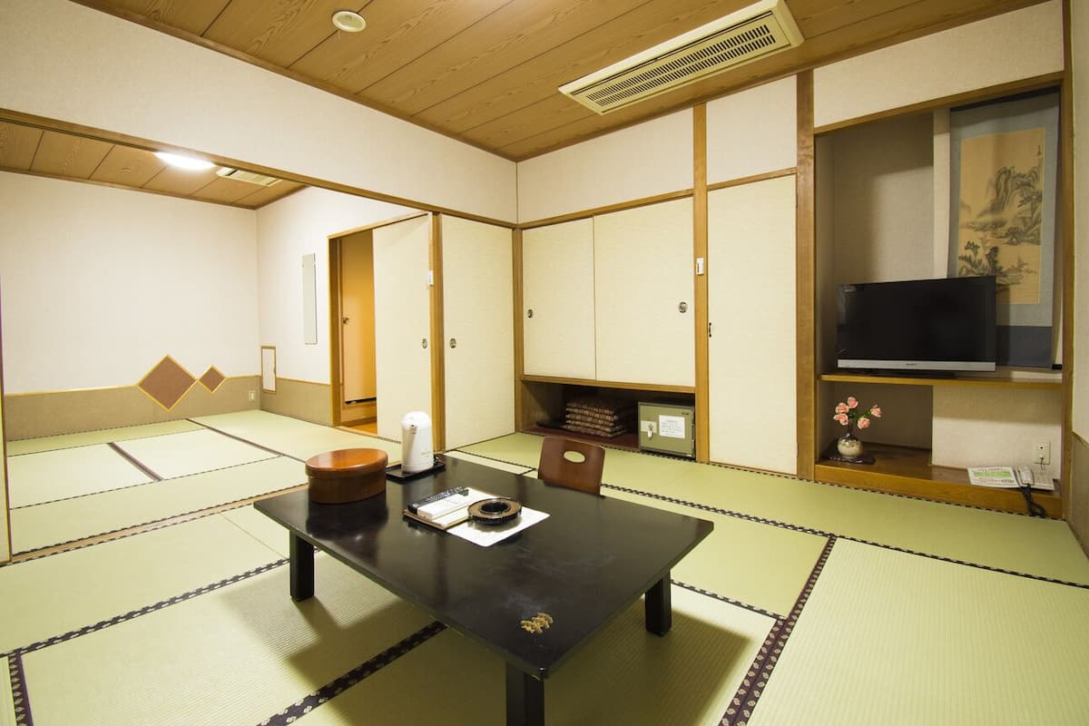 A traditional Japanese room with tatami flooring, a low table, a television, and a shelf with decorative items.