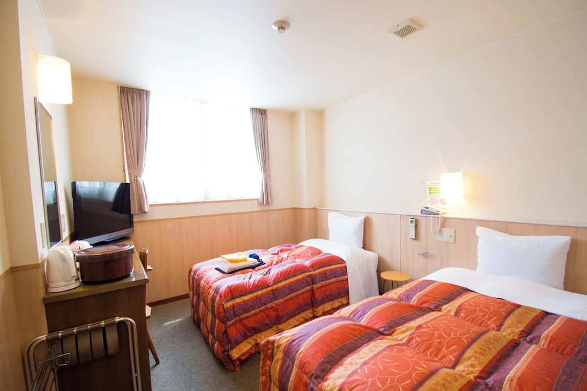 A hotel room with two beds, a TV, a desk with a lamp, and a window with curtains.