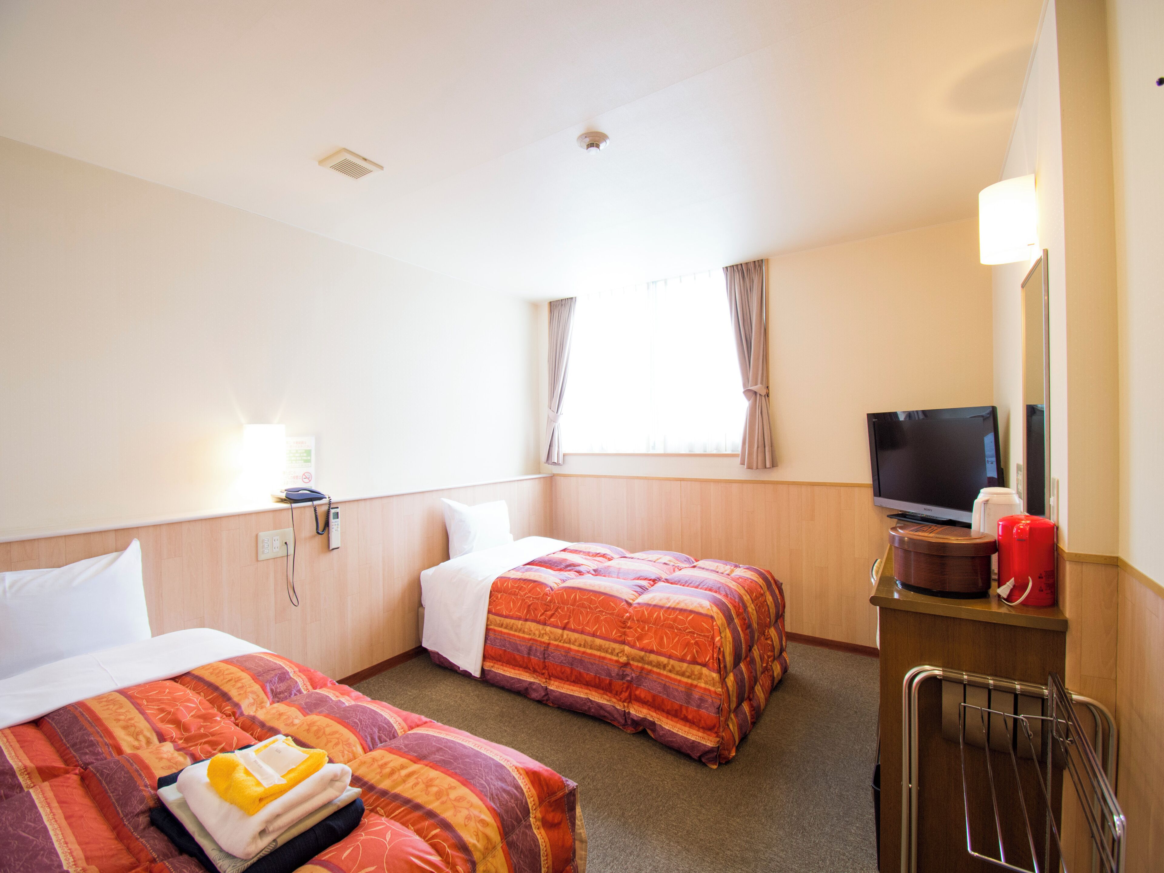 A hotel room with two beds, a TV, a desk with a coffee maker, and a window with curtains.