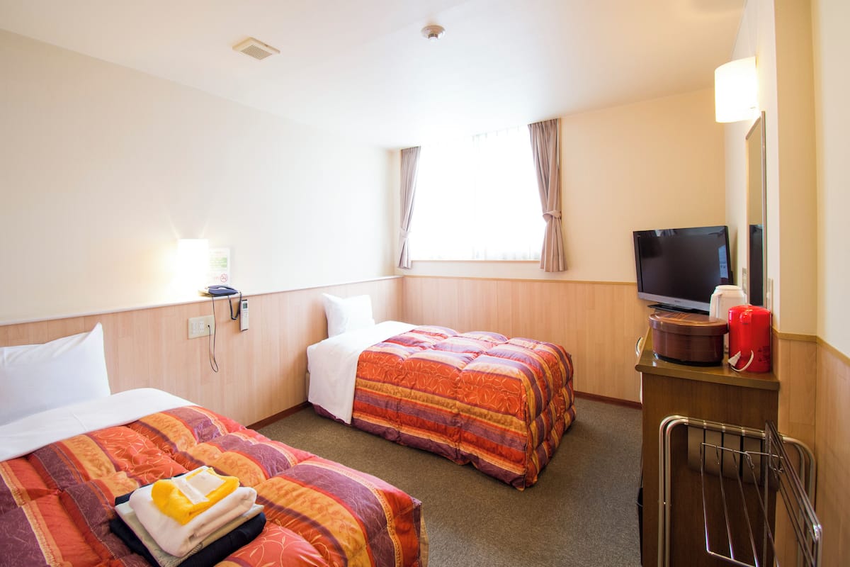 A hotel room with two beds, a TV, a desk with a coffee maker, and a window with curtains.