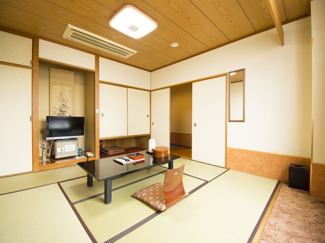 Ein traditioneller japanischer Raum mit Tatami-Bodenbelag, einem niedrigen Tisch, einem Fernseher und Schiebetüren.