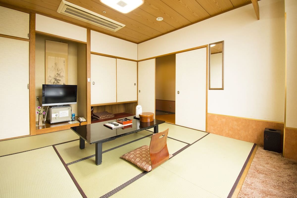 A traditional Japanese room with tatami flooring, a low table, a television, and sliding doors.