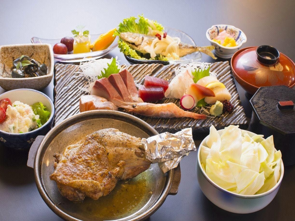 Variedad de platos, incluyendo un muslo de pollo asado, verduras y un bol con lo que parecen verduras encurtidas.