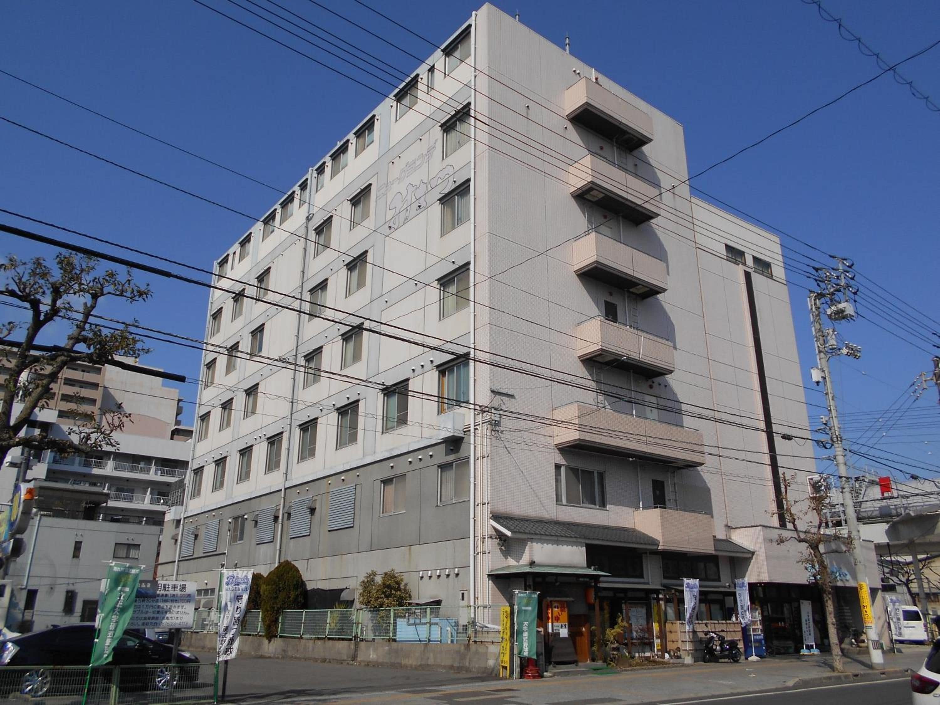 Un edificio de varios pisos con fachada plana, varios balcones y una entrada principal a nivel de calle con señalización.