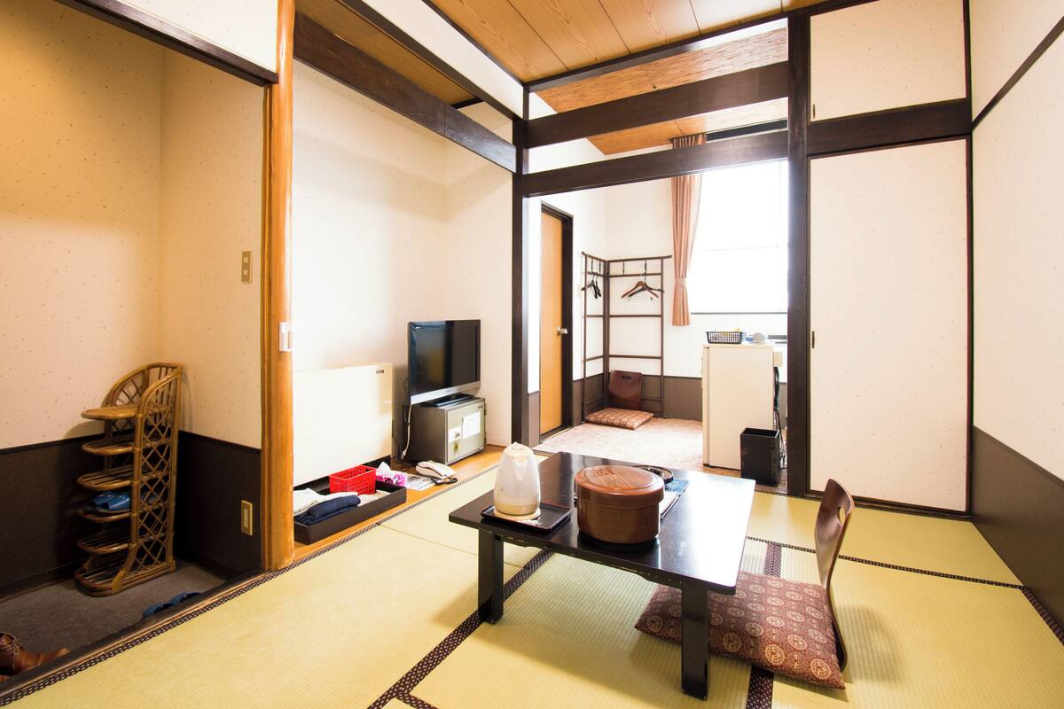 A traditional Japanese room with tatami flooring, a low table, a television, and a futon bed.