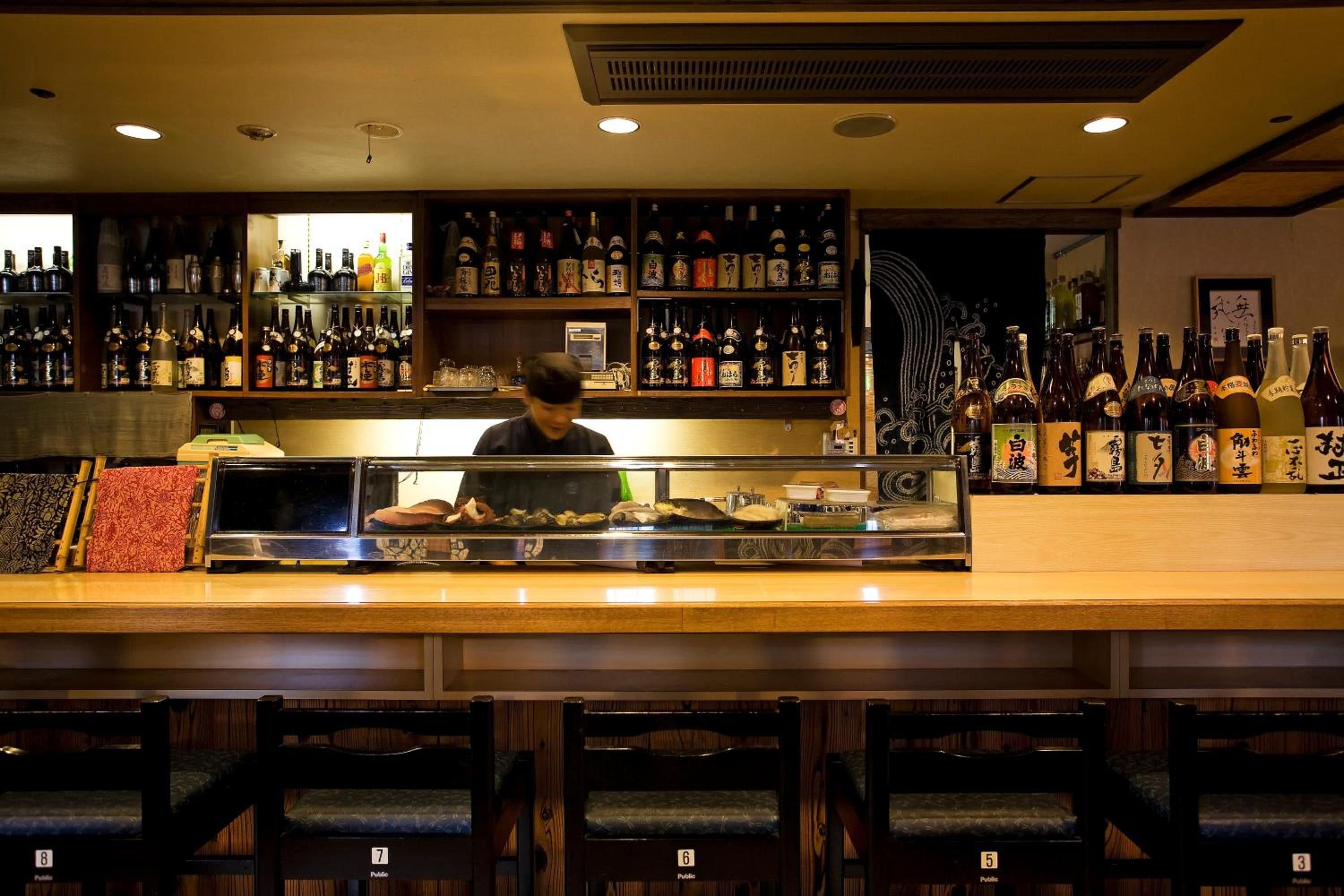 A bar with a counter, shelves of bottles, and chairs.