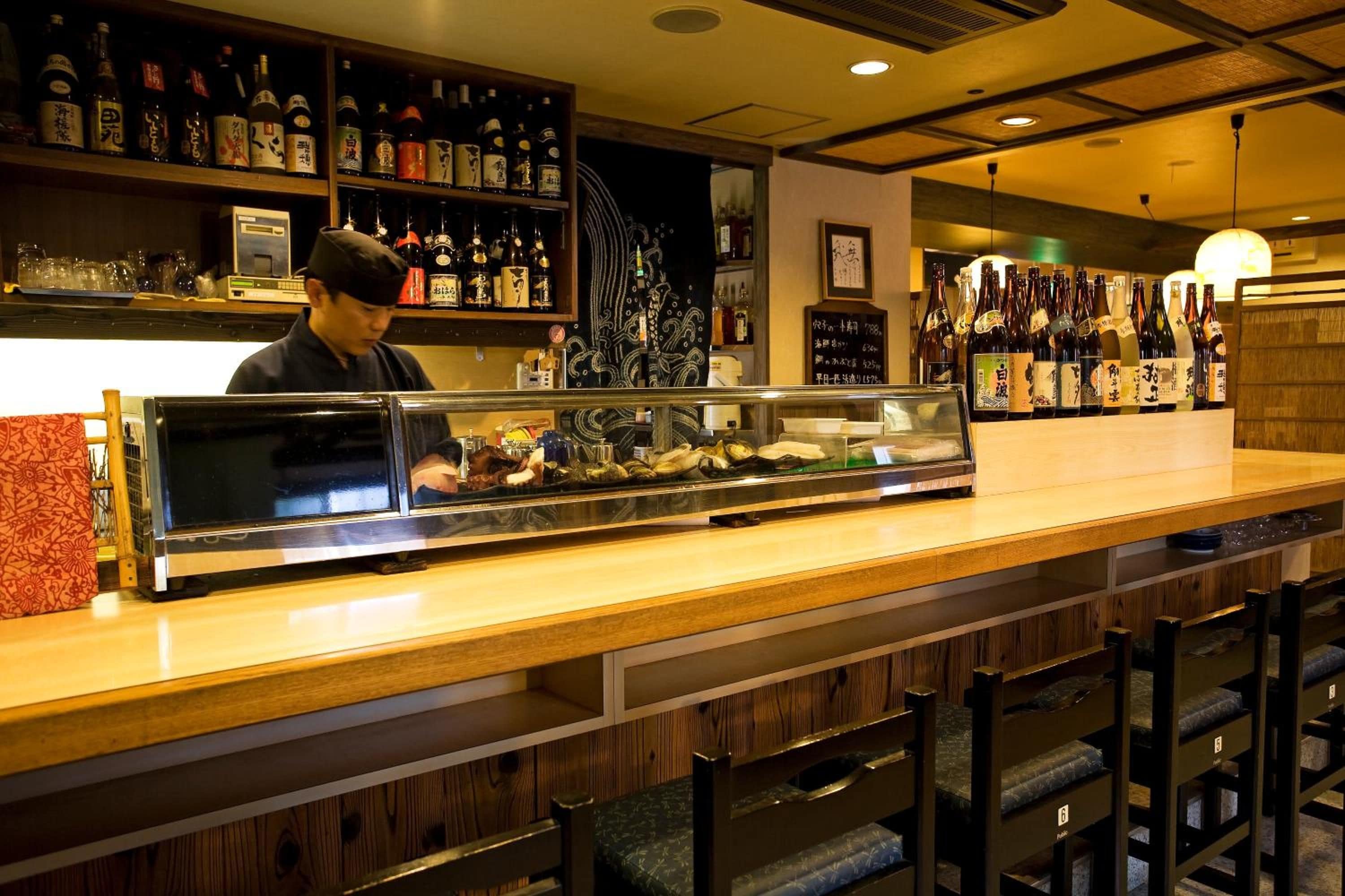 A bar area with shelves of bottles, a display case with food items, and a counter with a person behind it.