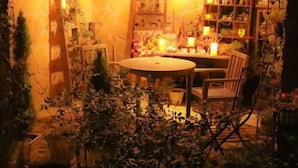 An indoor garden with a round table and chairs, surrounded by shelves with various items and plants.