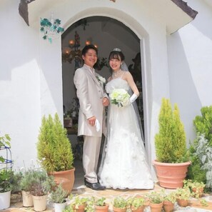 Ein Brautpaar in Hochzeitskleidung steht vor einem Eingang mit Blumentöpfen.