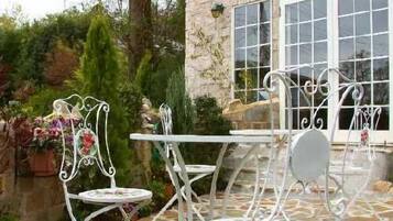 Un patio con sillas y mesa de metal blanco, rodeado de piso de piedra y follaje.