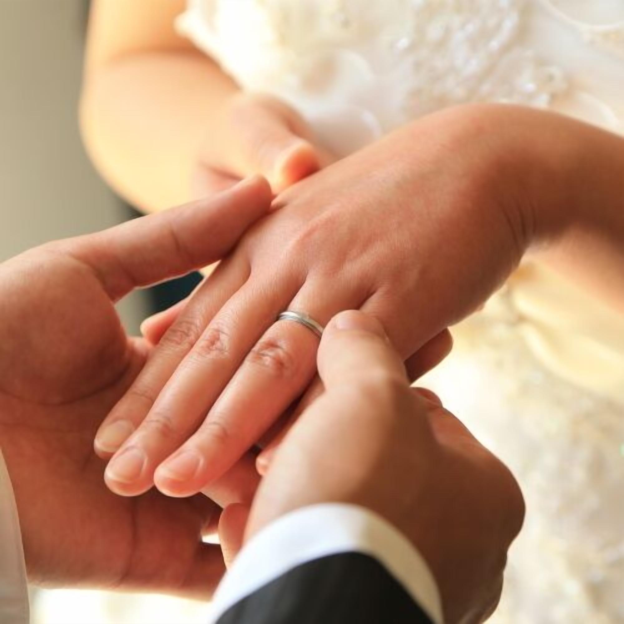 A close-up of hands holding a wedding ring.