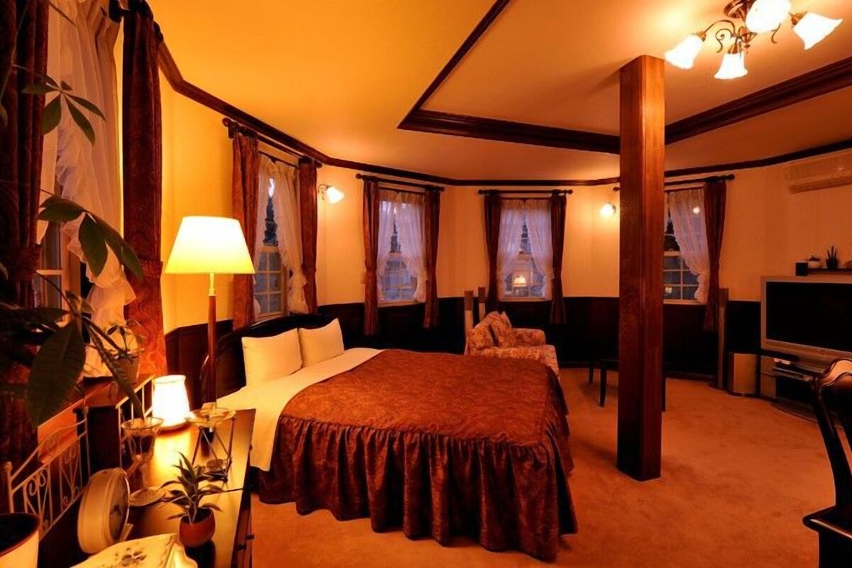A hotel room with a large bed, a desk with a TV, and a chandelier.