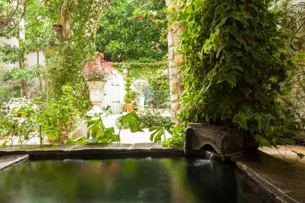 A tranquil indoor garden with a small water feature, stone walls, and lush greenery.