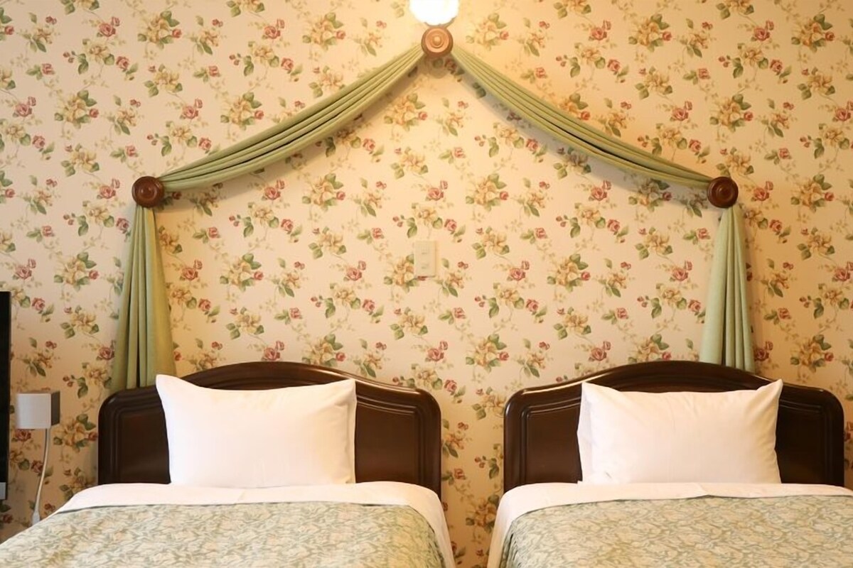 A room with two beds, floral wallpaper, and a canopy bed.
