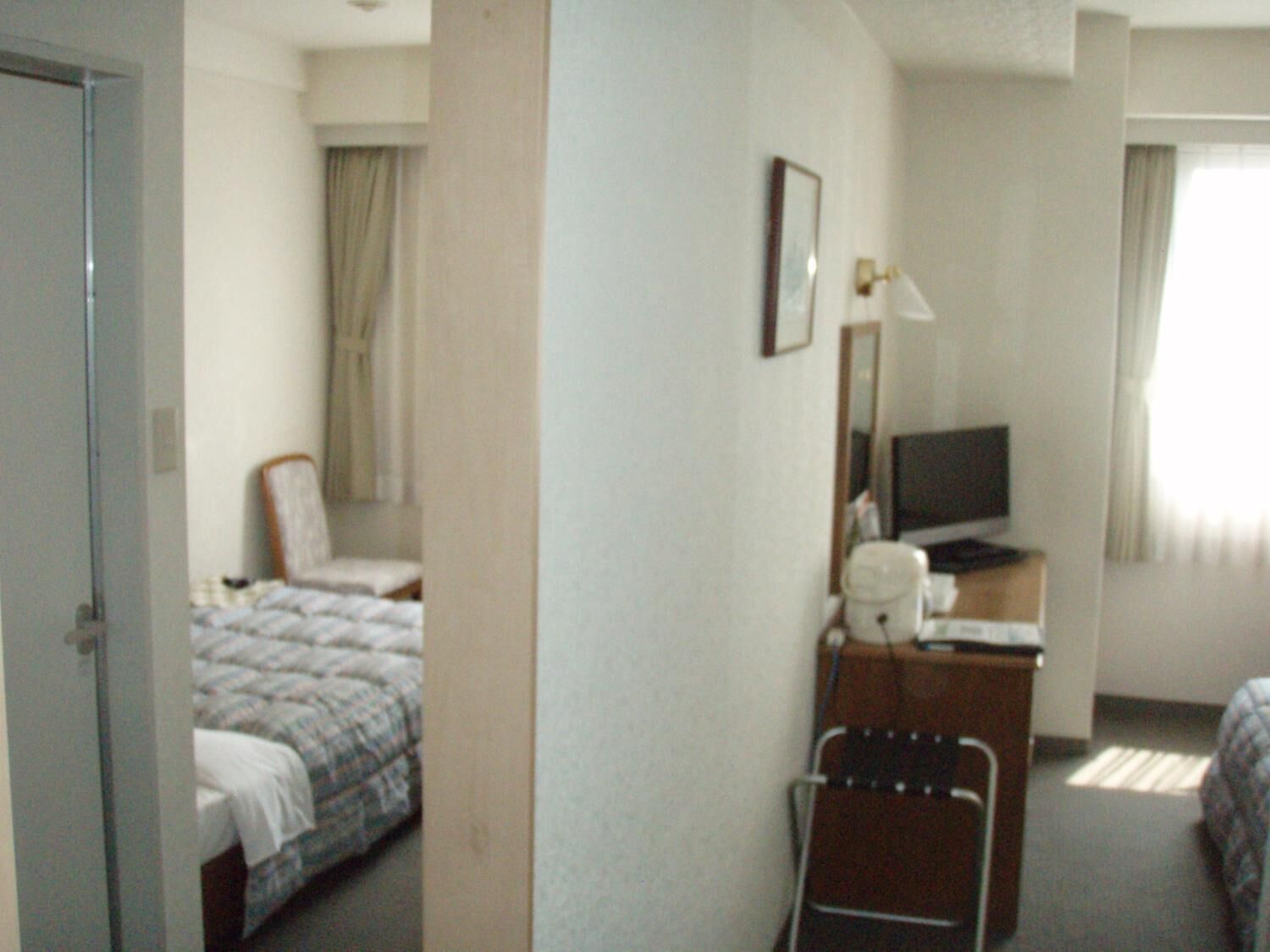 Une chambre d’hôtel avec un lit, une chaise, un bureau avec une télévision et une fenêtre avec des rideaux.