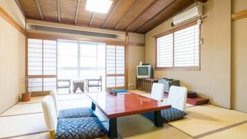 A tatami mat room with a low table, chairs, a television, and sliding doors.