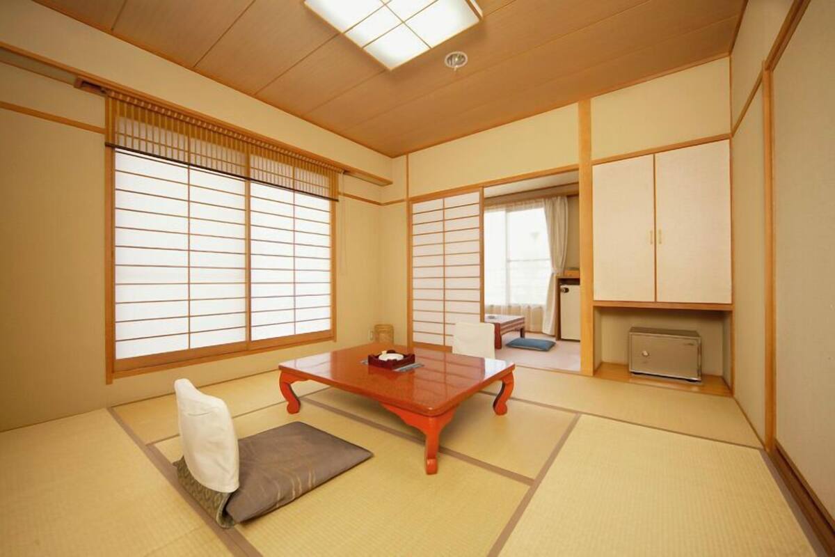 A traditional Japanese room with tatami flooring, sliding shoji doors, a low wooden table, and a futon bed.