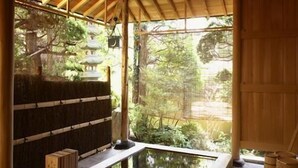 A traditional Japanese onsen with a wooden bath, a stone platform, and a view of a forested area.
