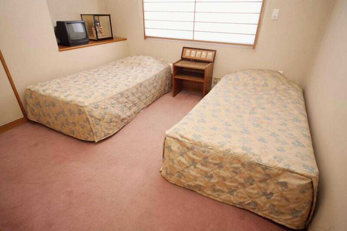 A room with two beds, a television, and a small wooden shelf with pictures.