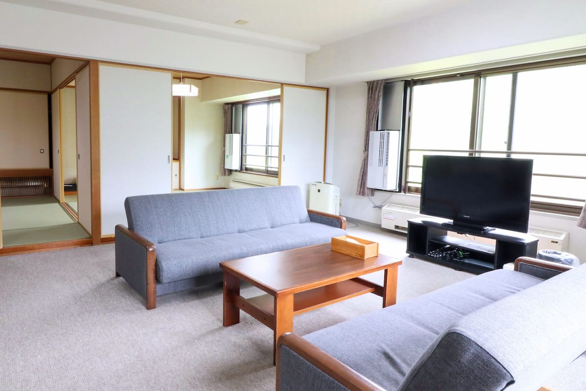 A living room with a sofa, a coffee table, a television, and a sliding door leading to a bathroom.