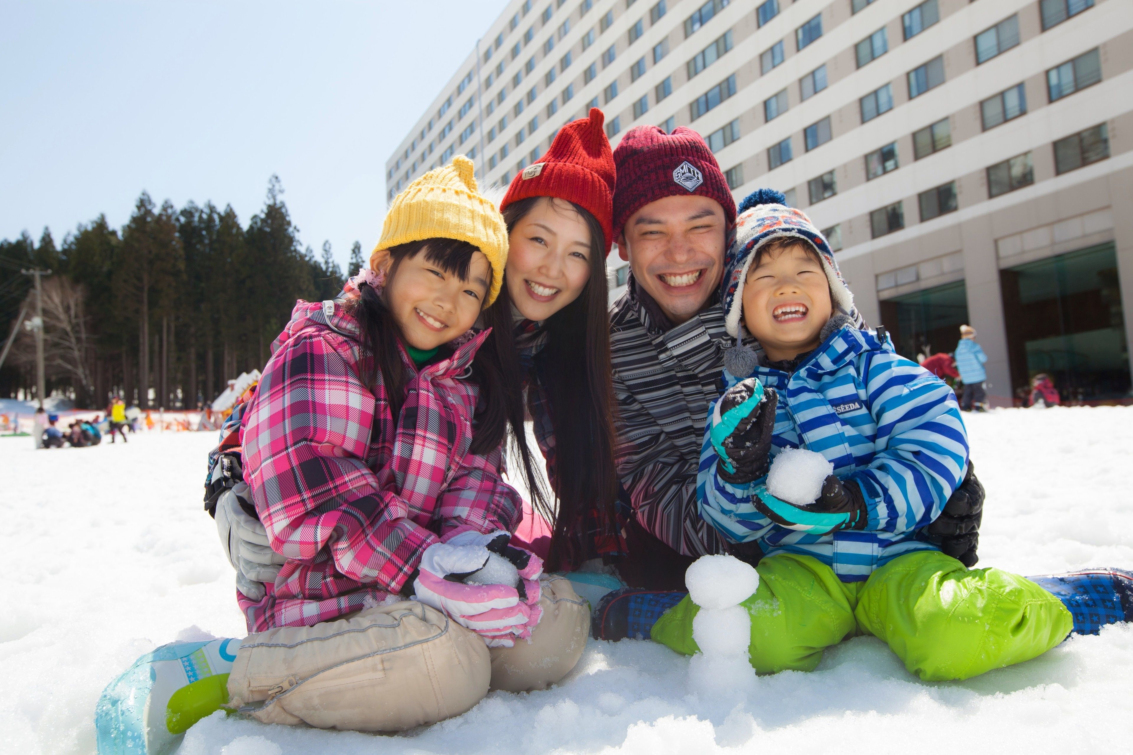 A group of people sitting on snow in front of a building.