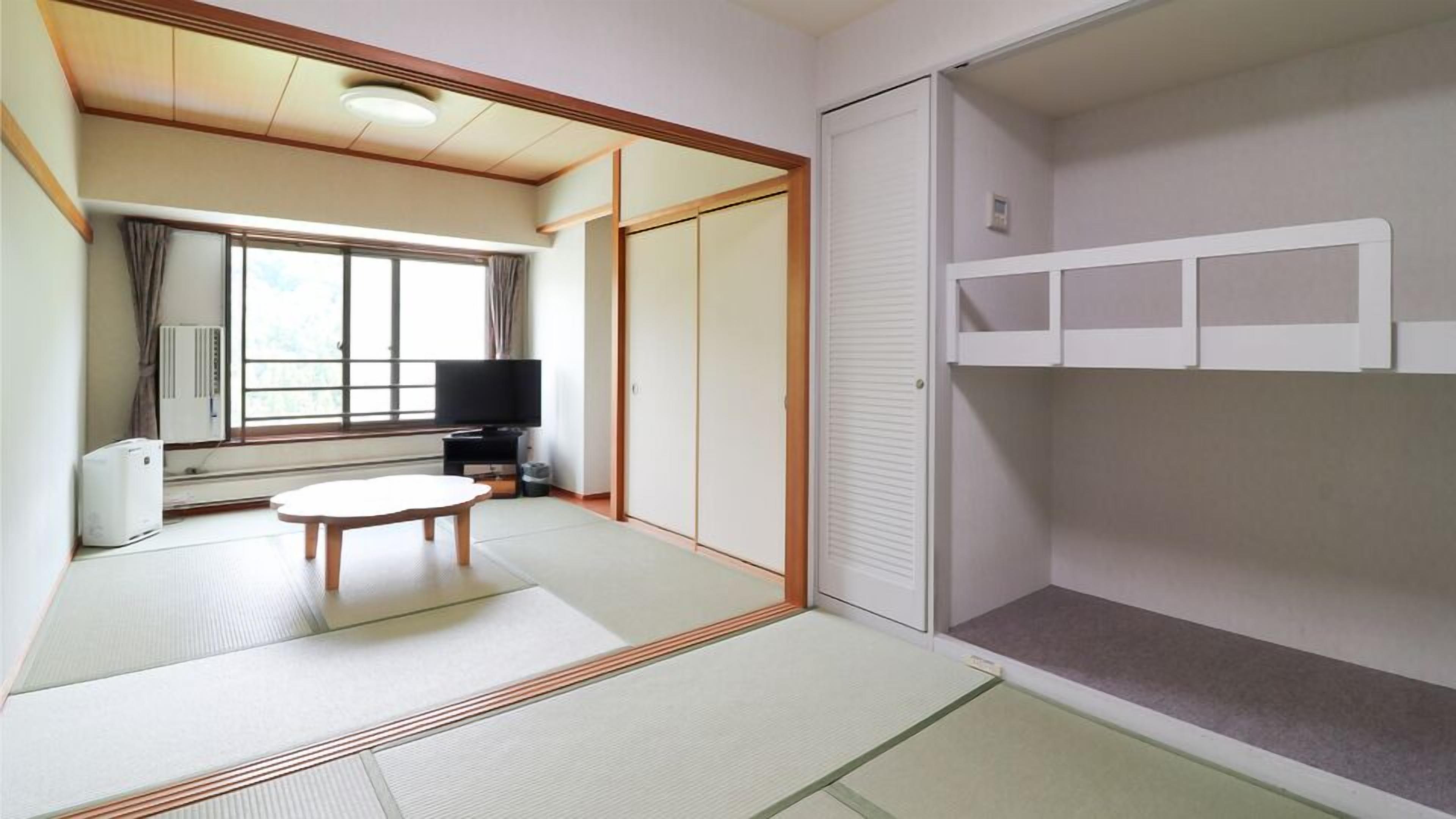 Une pièce avec un sol recouvert de tatamis, une table basse en tatami, un téléviseur et des portes coulissantes.