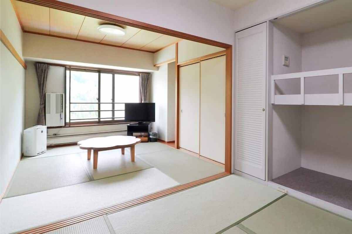 A room with tatami flooring, a tatami mat table, a television, and sliding doors.