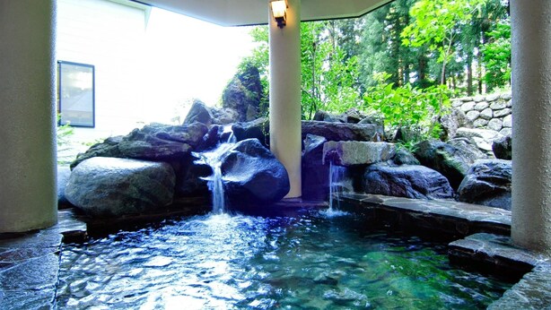Um elemento aquático tranquilo em ambiente interno, com uma cascata de pedra, rodeado por pedras e vegetação.
