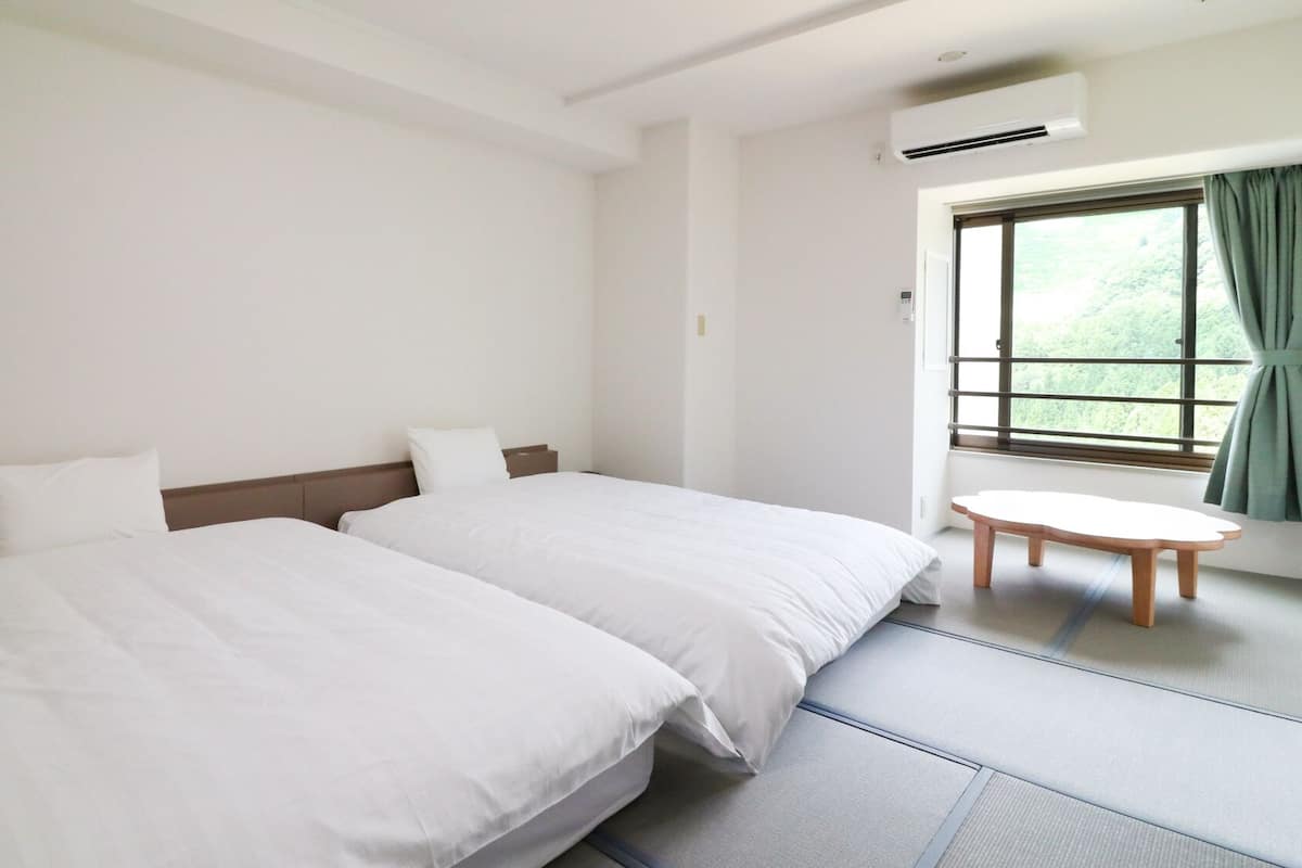A hotel room with two beds, a small round table, and a window with curtains.