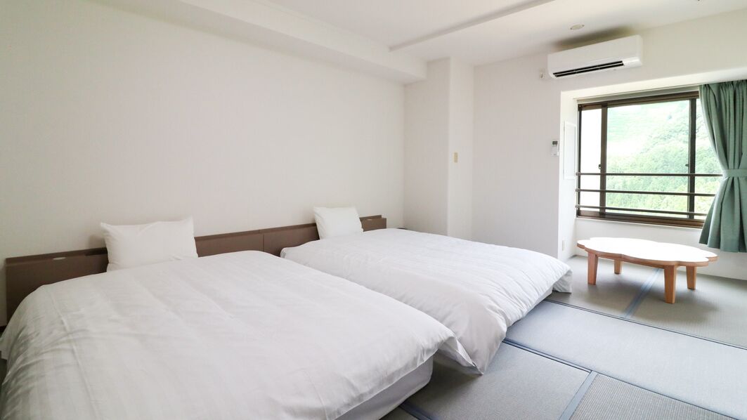 Une chambre d’hôtel avec deux lits, une petite table ronde et une fenêtre avec des rideaux.