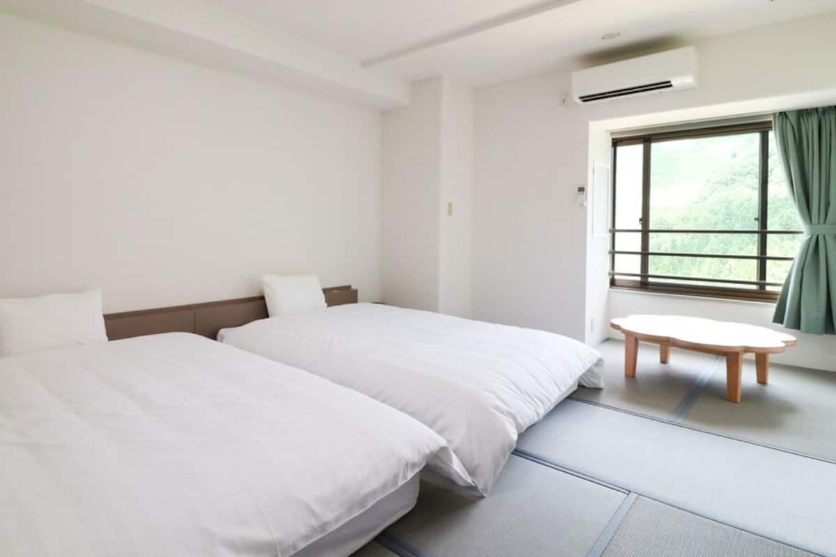 A hotel room with two beds, a small round table, and a window with curtains.