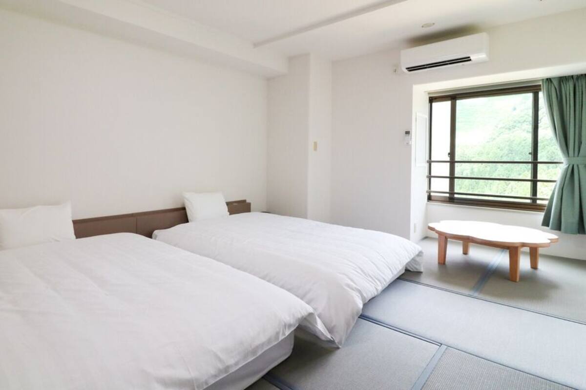 Une chambre d’hôtel avec deux lits, une petite table ronde et une fenêtre avec des rideaux.