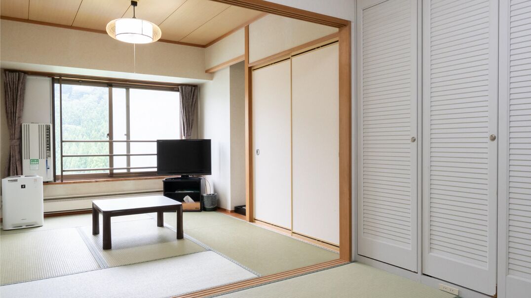 Une pièce de style japonais traditionnel, avec un sol recouvert de tatamis, un téléviseur, un radiateur et des portes coulissantes.