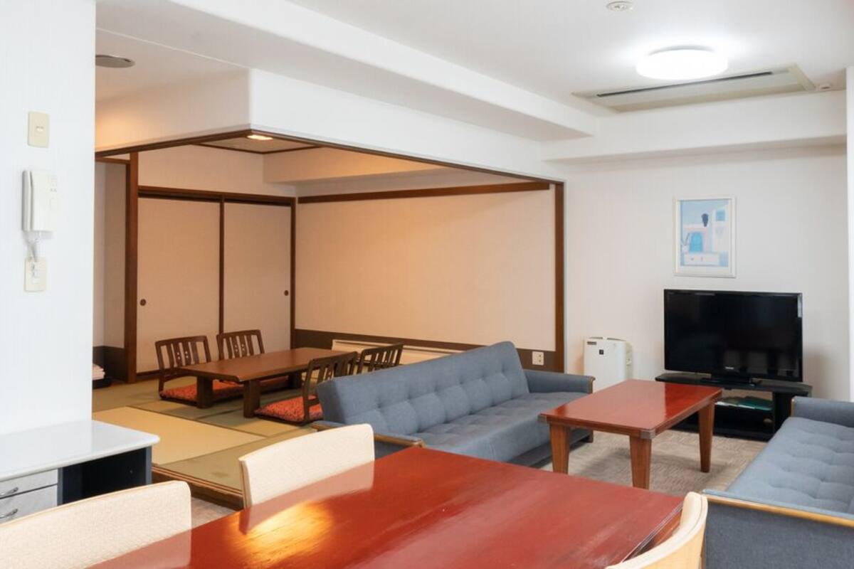 A modern living room with a sofa, a coffee table, a TV, and a dining area with chairs and a table.