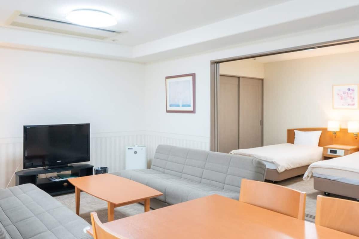 A hotel room with a sofa, two single beds, a TV, a desk, and a lamp.