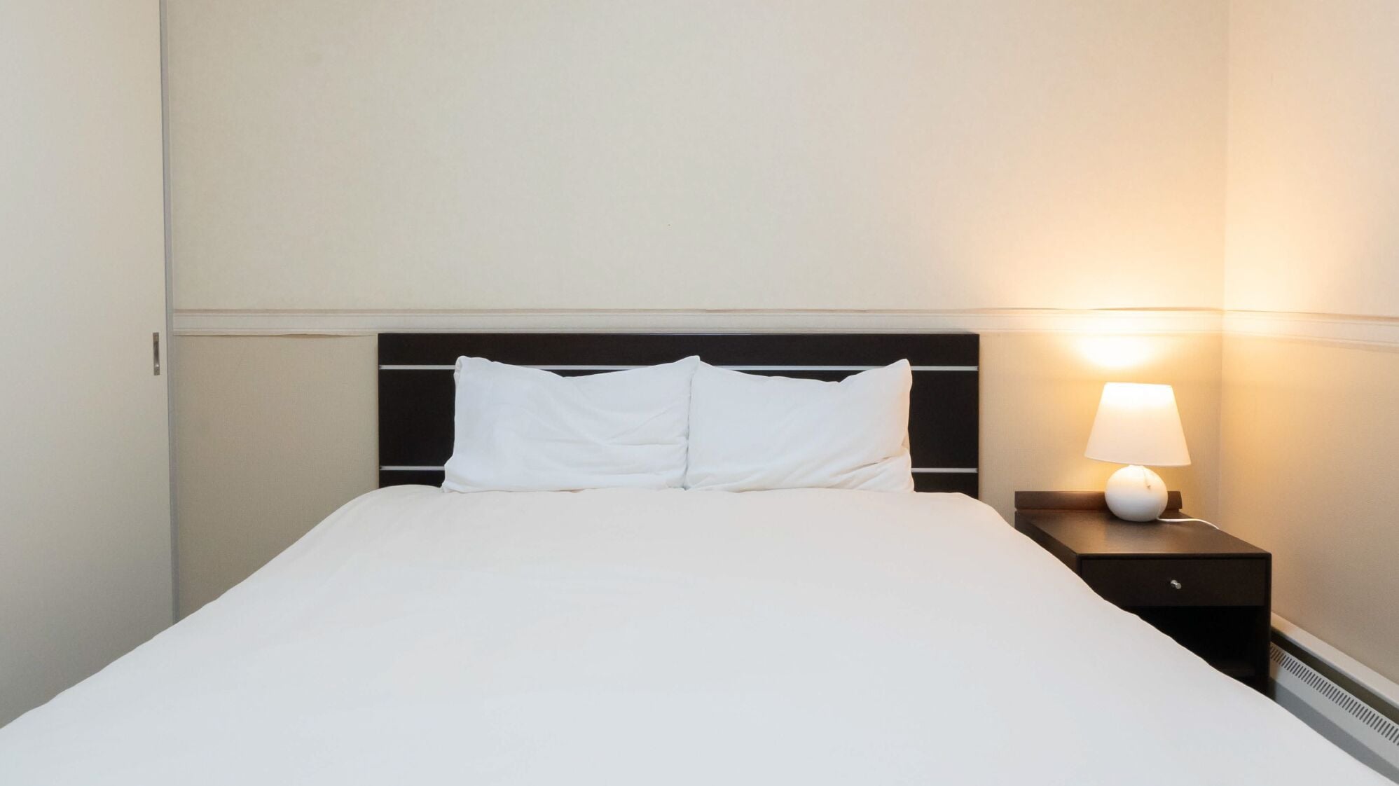 A neatly made bed with white linens, a black headboard, and a bedside lamp on a nightstand.